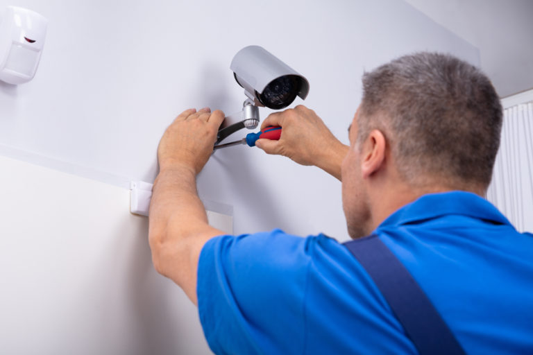 Close-up Of Male Technician Adjusting Cctv Camera On Wall With Screwdriver